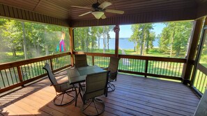 A covered outdoor area with a table and chairs, a ceiling fan, and a view of a golf course and lake.