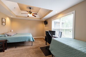 A bedroom with two beds, a ceiling fan, a desk, and a window with blinds.