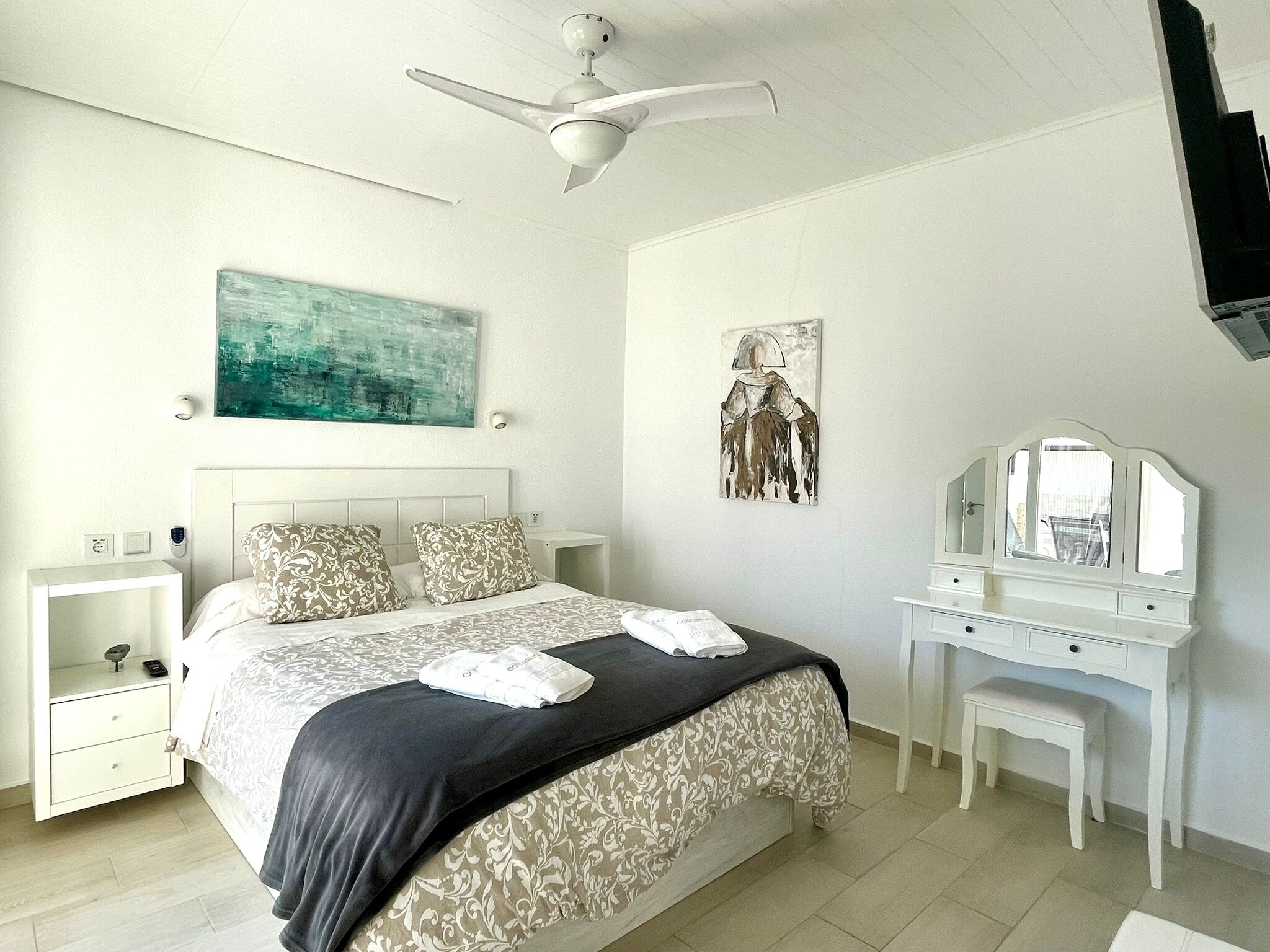 A bedroom with a bed, nightstands, a dresser, a ceiling fan, and artwork on the walls.