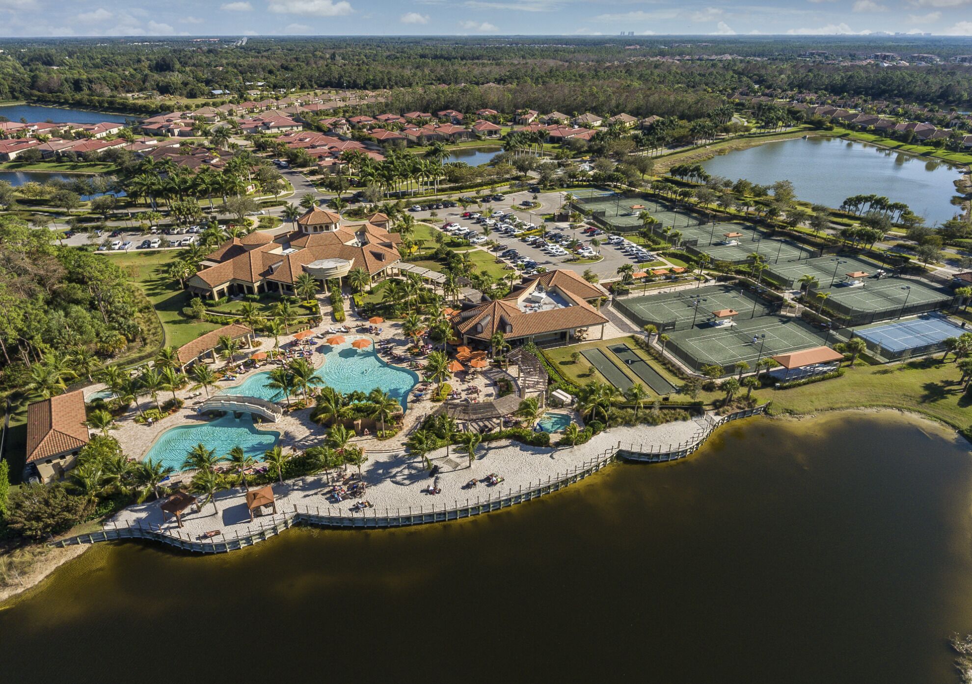 Luchtbeeld van een resort met meerdere zwembaden, tennisbanen en een strandgedeelte.