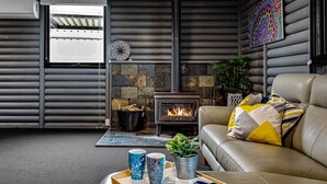 A cozy living room with a stone fireplace, a leather sofa, and a coffee table with mugs and a plant. - Silvers Anchor - 2 Bennett Street (CARRICKALINGA)