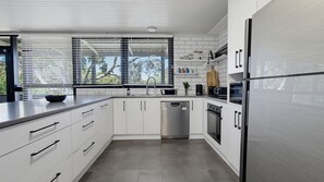 A modern kitchen with white cabinetry, stainless steel appliances, and a window with blinds. - Silvers Anchor - 2 Bennett Street (CARRICKALINGA)