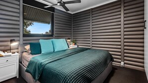 A bedroom with a bed, a nightstand, a lamp, a ceiling fan, and a window. - Silvers Anchor - 2 Bennett Street (CARRICKALINGA)