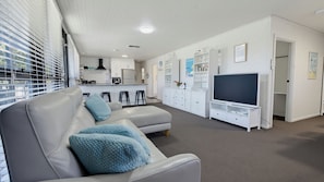 A modern living room with a sofa, a TV stand, and a kitchen area in the background. - Silvers Anchor - 2 Bennett Street (CARRICKALINGA)