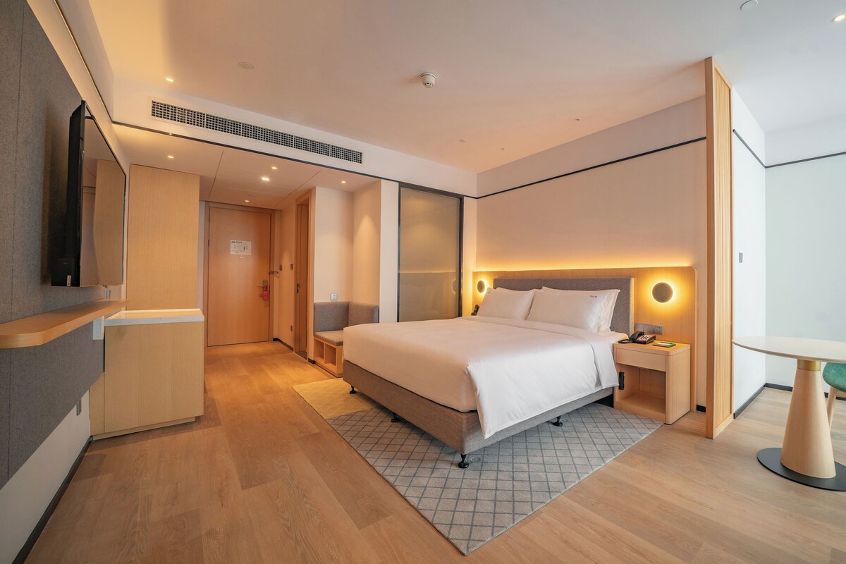 A modern hotel room with a large bed, bedside table, and a green chair.