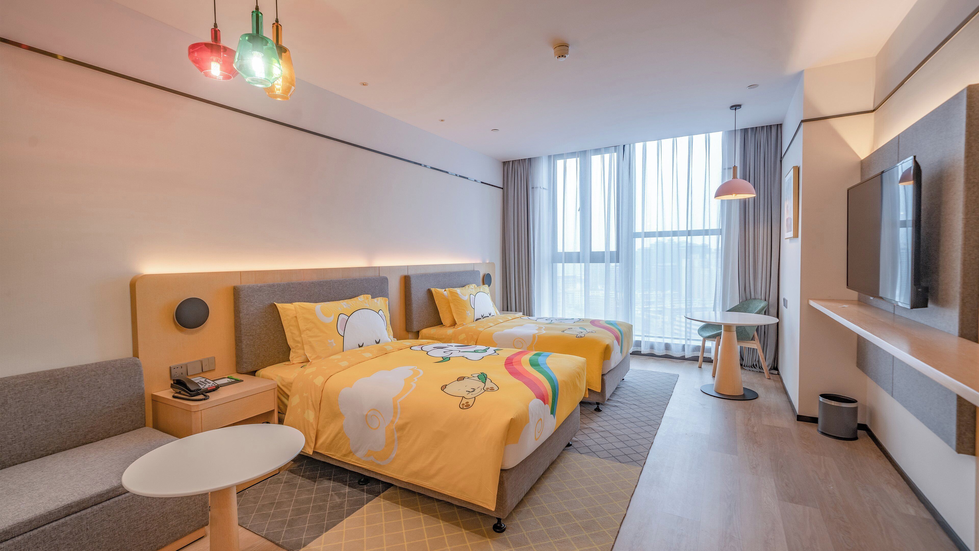 Una habitación de hotel con cama, mesitas de noche, un sofá, televisor y ventana con cortinas.