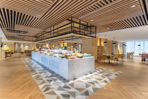 Eine moderne Hotelhalle mit einem zentralen Buffet, Holzboden und einem geometrisch gemusterten Teppich.