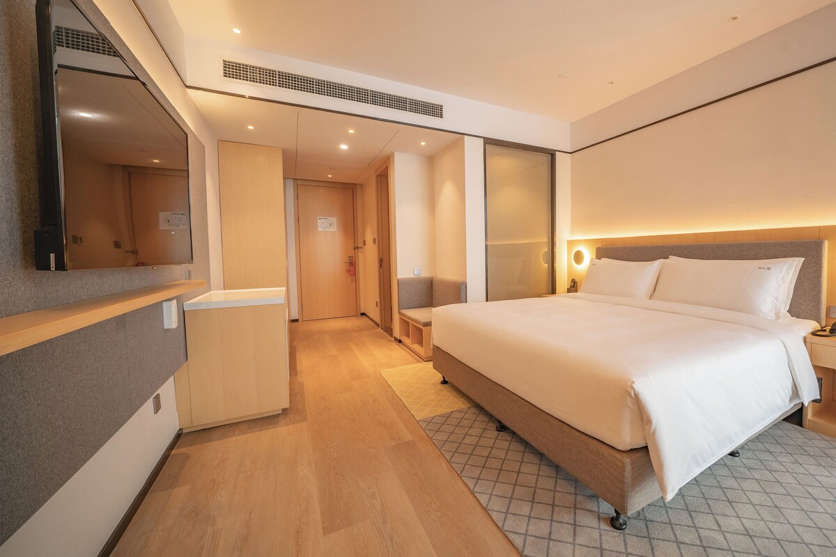 A modern hotel room with a large bed, bedside tables, a desk, and a mirror.