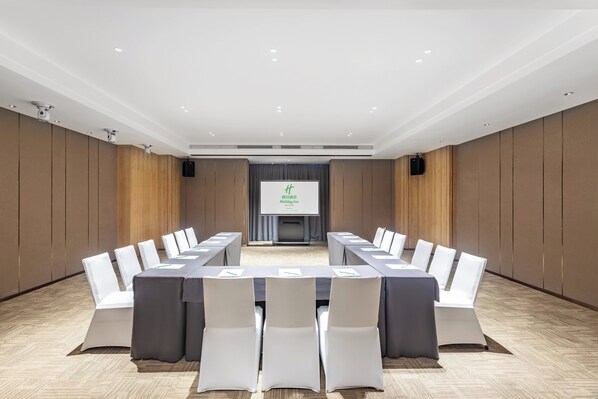 A conference room with a long table, white chairs, and a presentation screen.