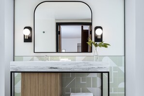 Een badkamer met een marmeren wastafel, een grote spiegel en twee wandlampen.
