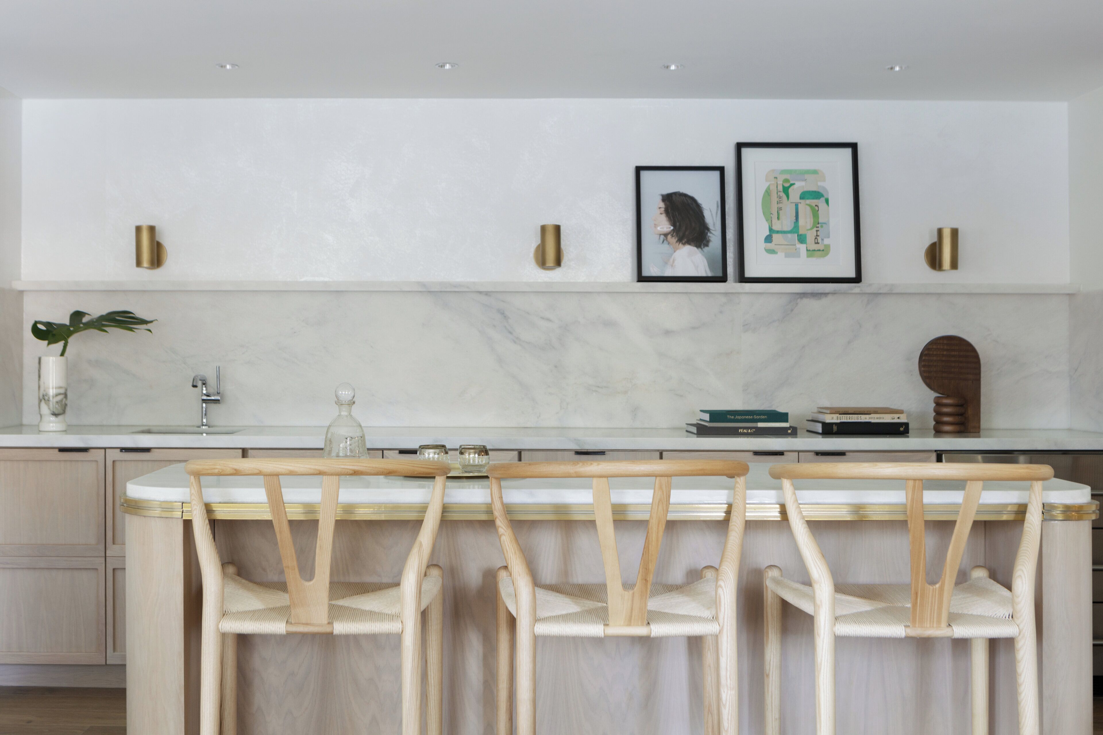 Une cuisine moderne avec un plan de travail en marbre, des chaises en bois et des œuvres d’art encadrées accrochées au mur.