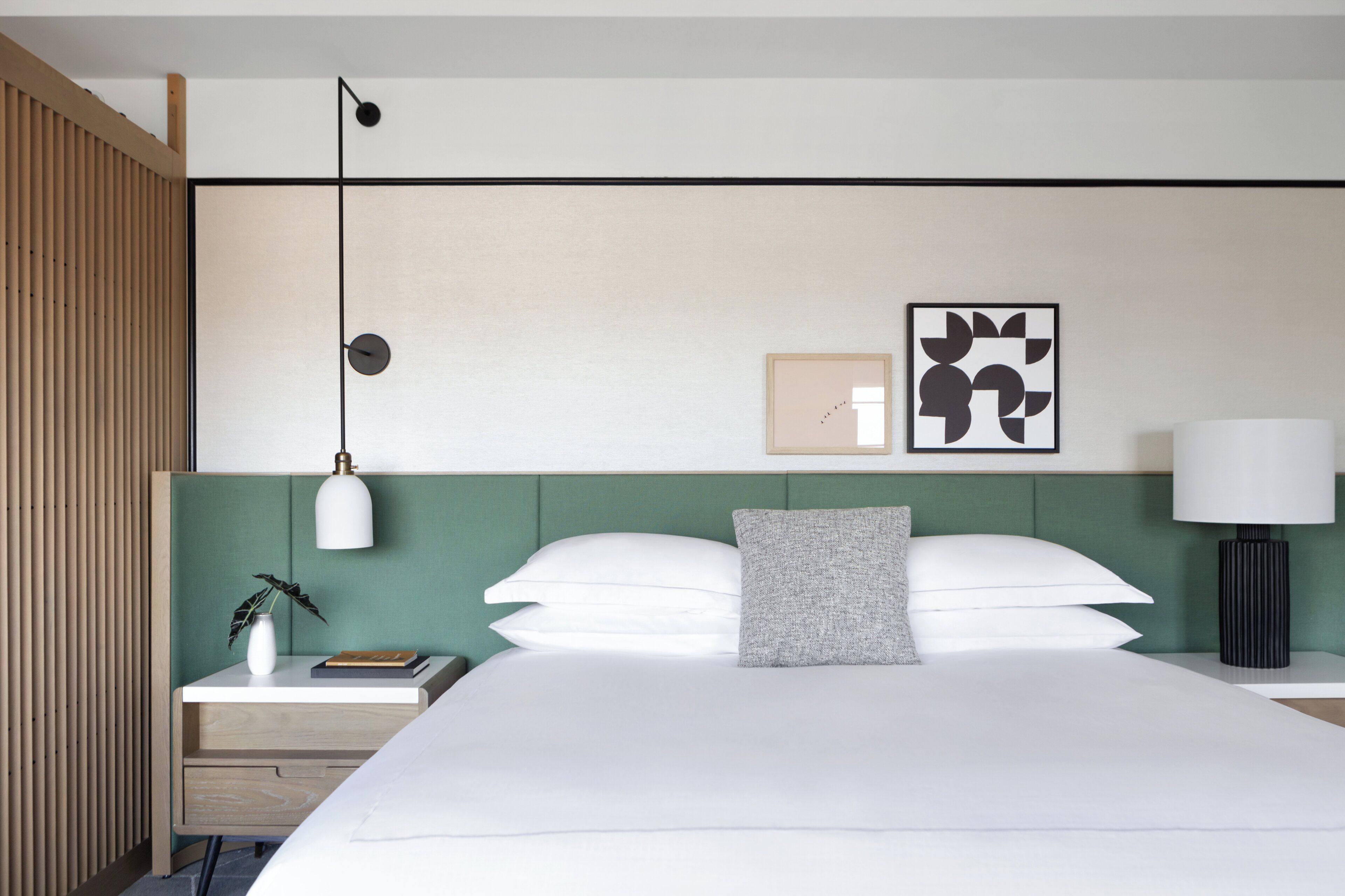 Et moderne hotelværelse med en stor seng, et natbord med lampe, et billede på væggen og et vindue med persienner.