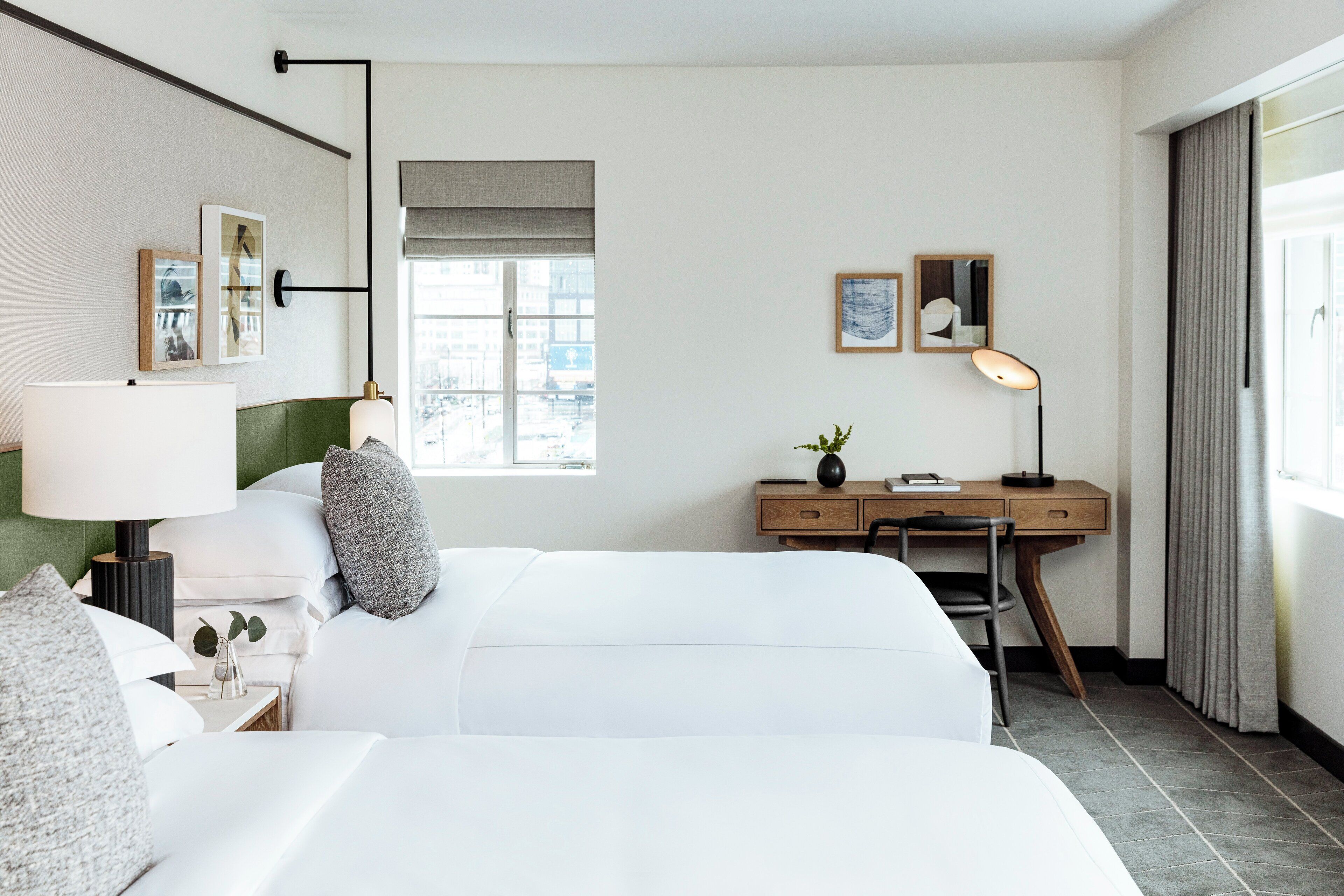 A hotel room with a bed, a desk, a chair, a lamp, and a window.