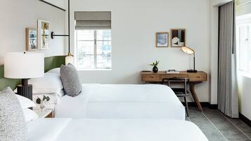A hotel room with a bed, a desk, a chair, a lamp, and a window.