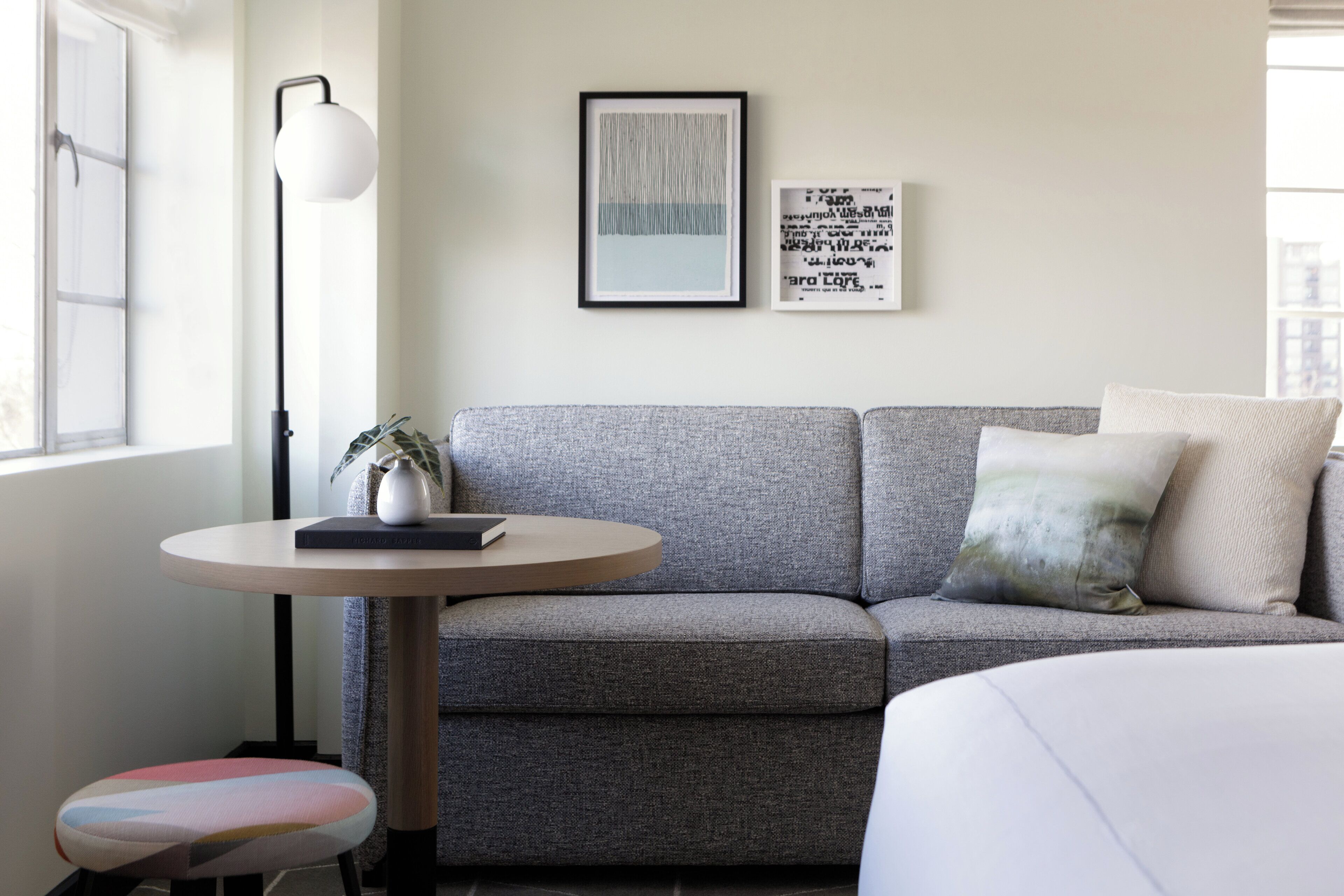 A modern living room with a grey sofa, a round wooden table, a floor lamp, and a small plant.