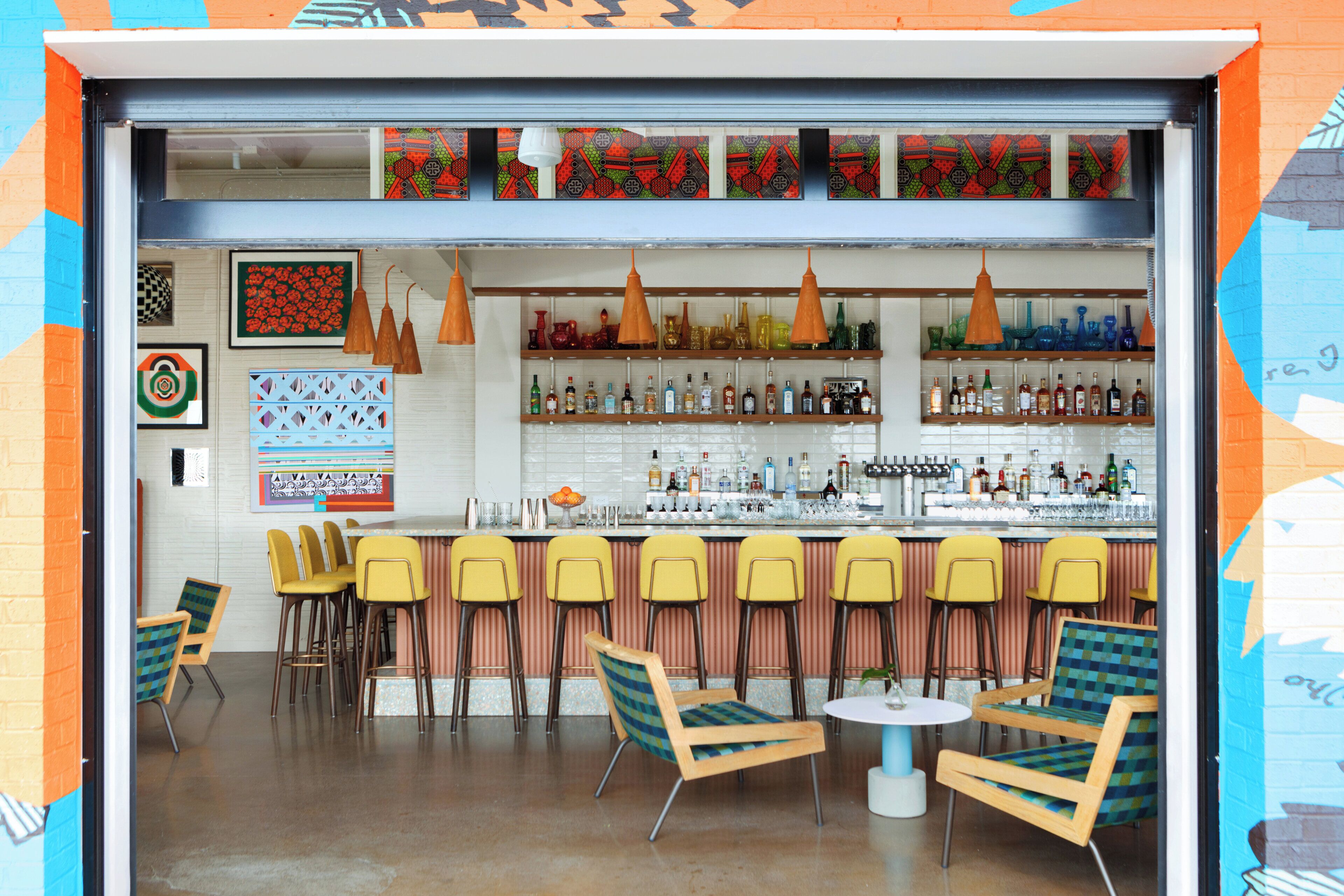 A bar area with multiple seating options, including bar stools and chairs, and a variety of bottles and glasses on shelves.
