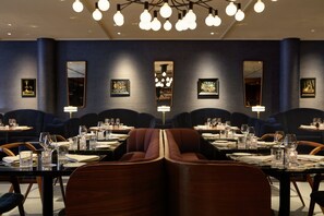 Ein Restaurant mit modernem Interieur, gekennzeichnet durch dunkelblaue Wände, mehrere Kronleuchter und gerahmte Kunstwerke an den Wänden.