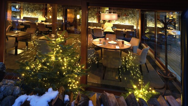 A two-story chalet with a balcony, a dining area with outdoor seating, and a Christmas tree with lights.