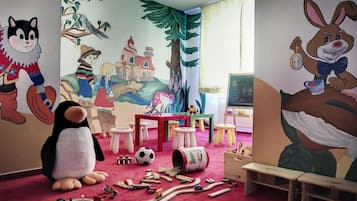 A child's playroom with a large stuffed penguin, a wooden train set, and colorful murals on the walls.