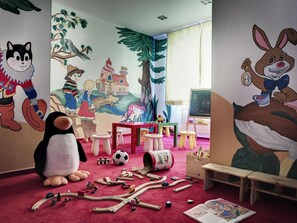 Una habitación infantil con un gran peluche de pingüino, un tren de madera y murales coloridos en las paredes.