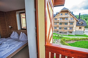 A bedroom with a wooden headboard, a bed with white bedding, and a window with blinds. - Aplend Kukucka Mountain Hotel & Residences (Vysoké Tatry)