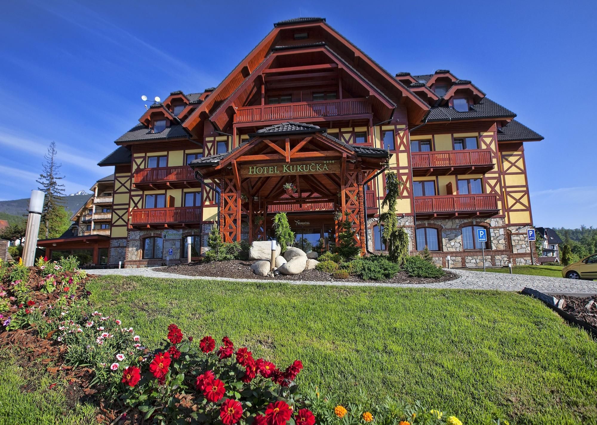A large hotel with a prominent entrance, multiple balconies, and a well-maintained garden with flowers.