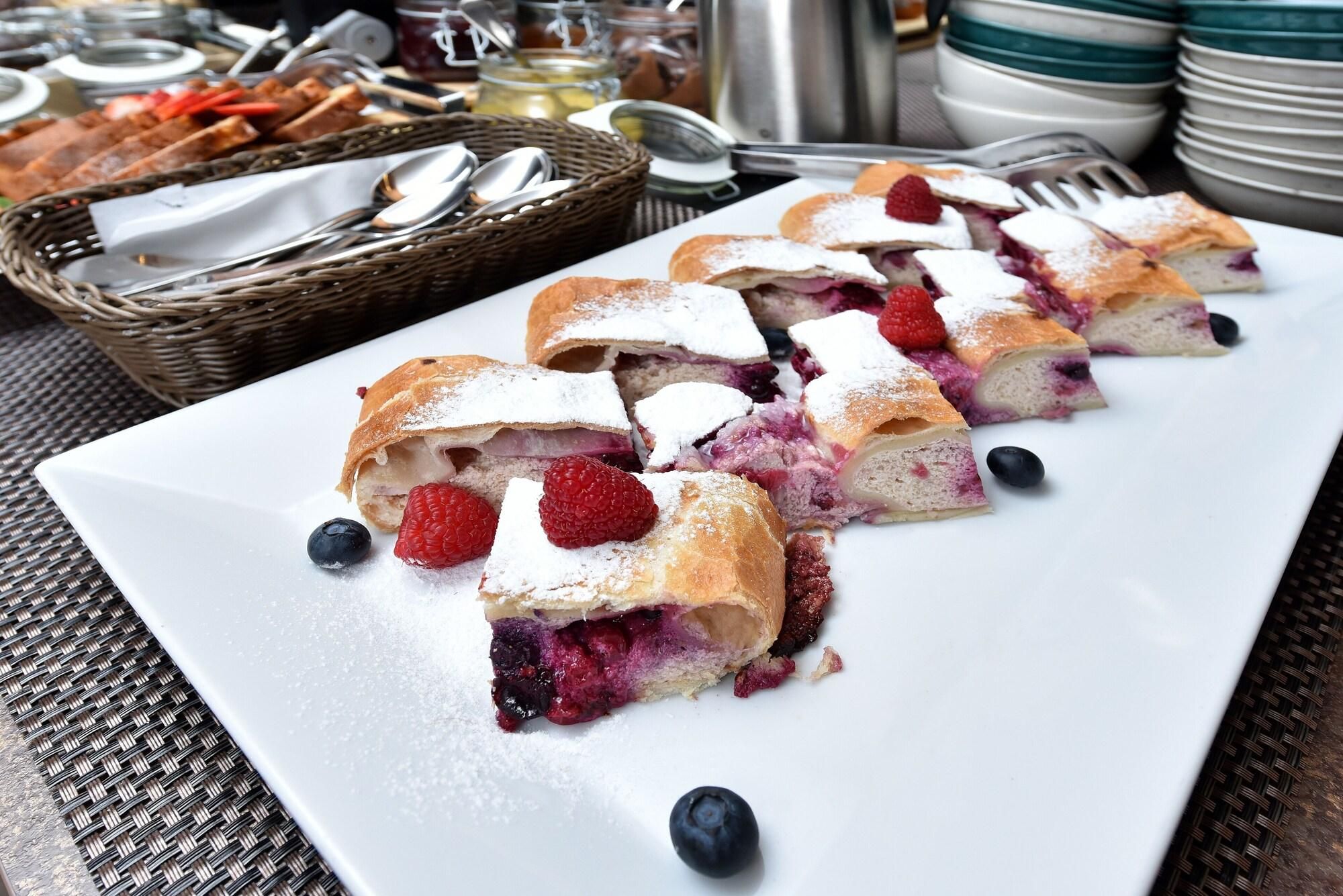 A plate of fruit-filled pastries with raspberries and blueberries, accompanied by a basket of bread and utensils.
