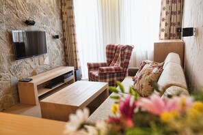 Una sala de estar con pared de piedra, un televisor de pantalla plana, un sillón a cuadros, un sofá y una mesa de centro de madera.