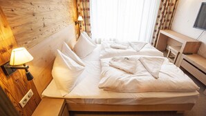 A hotel room with a wooden headboard, a bedside lamp, a bed with white linens, and a TV mounted on the wall.