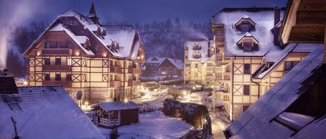 A traditional European village at night with snow-covered buildings and a lit street.