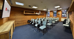 A conference room with rows of chairs, wooden walls, a projector screen, and windows with a view of trees. - Aplend Kukucka Mountain Hotel & Residences (Vysoké Tatry)