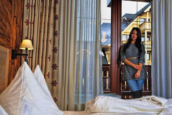 A hotel room with a bed, a window with curtains, and a view of buildings outside. - Aplend Kukucka Mountain Hotel & Residences (Vysoké Tatry)