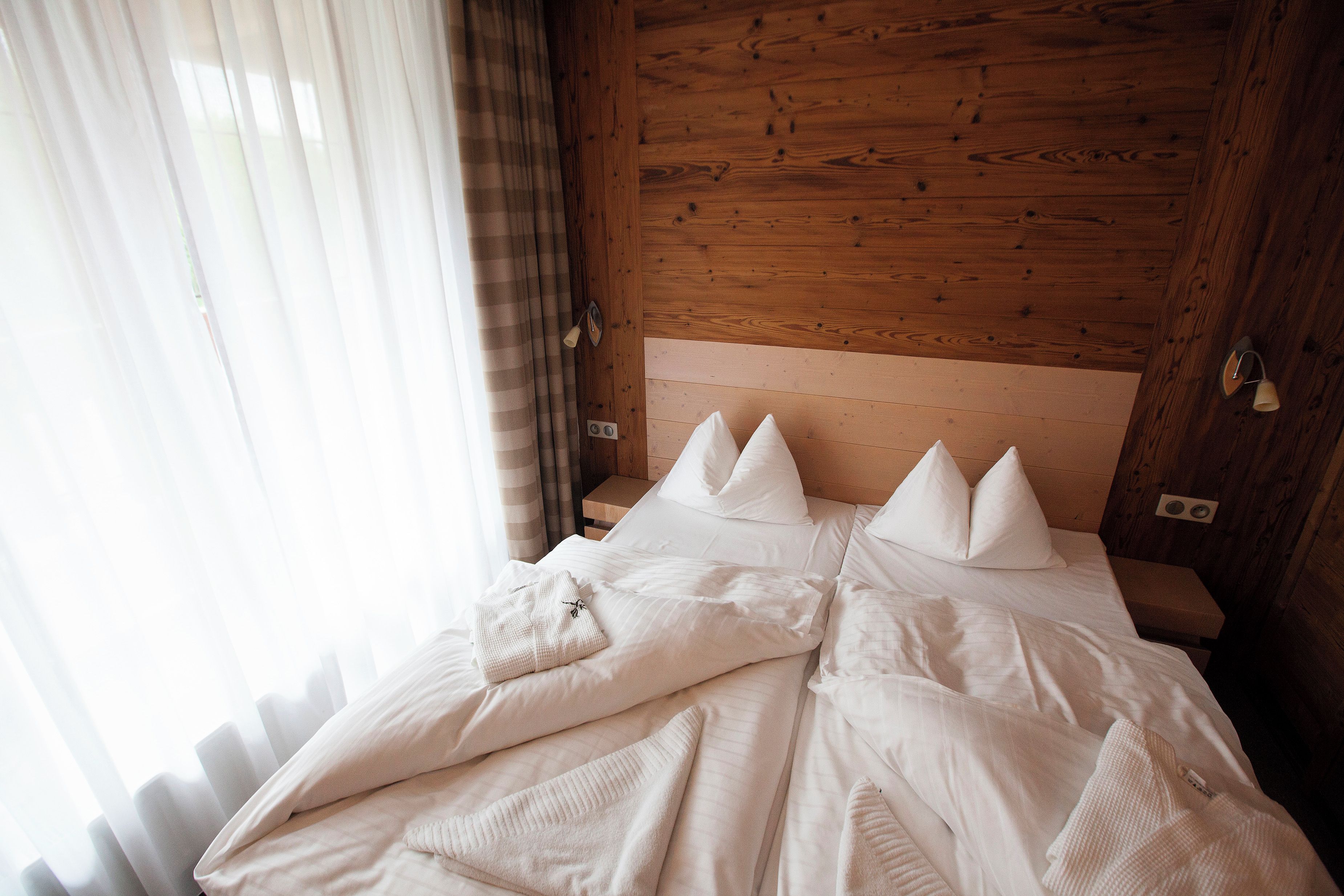 Una cama bien tendida con ropa blanca y almohadas, un cabecero de madera y una mesita de noche con una lámpara.