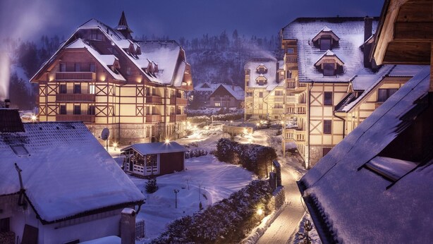 A traditional European village at night with snow-covered buildings and a lit street.