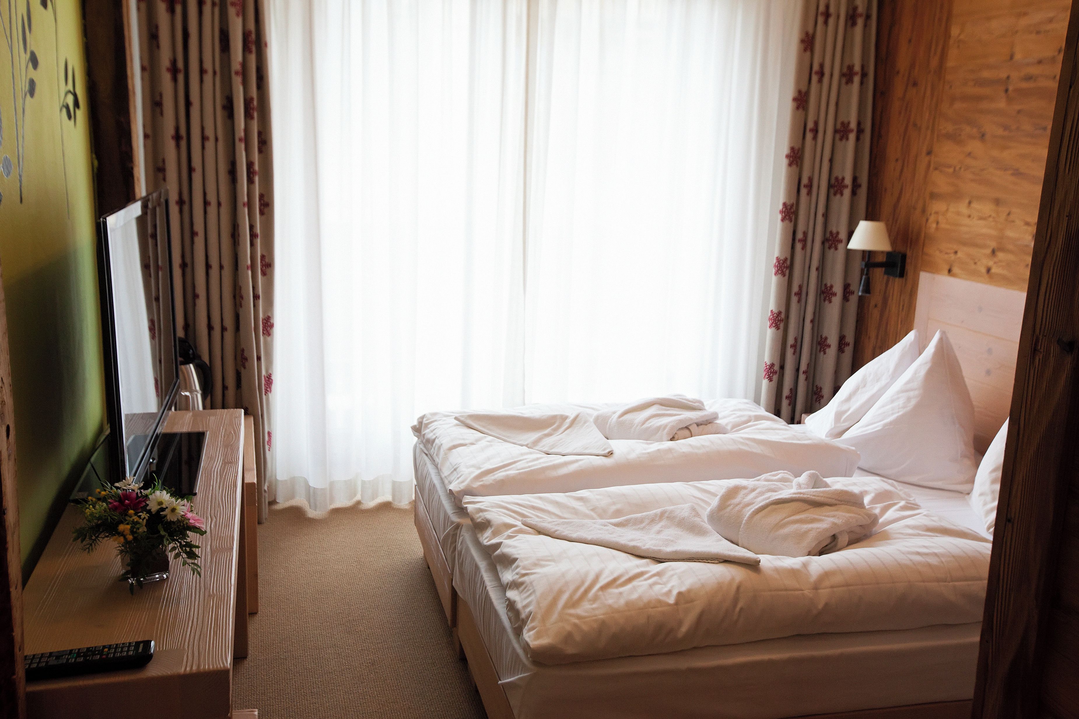 A hotel room with a bed, a TV, a remote control, and a lamp.