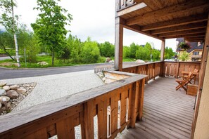 A wooden deck with a stone patio, outdoor seating, and a view of a road and greenery. - Aplend Kukucka Mountain Hotel & Residences (Vysoké Tatry)