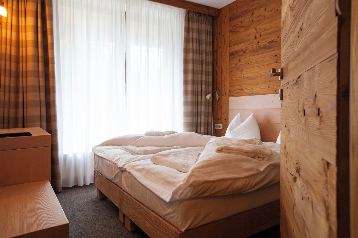 A neatly made bed with a wooden headboard, a bedside table, and a window with curtains.
