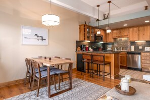 Une cuisine moderne avec des meubles en bois, un réfrigérateur en acier inoxydable et un coin repas comprenant une table et des chaises en bois.