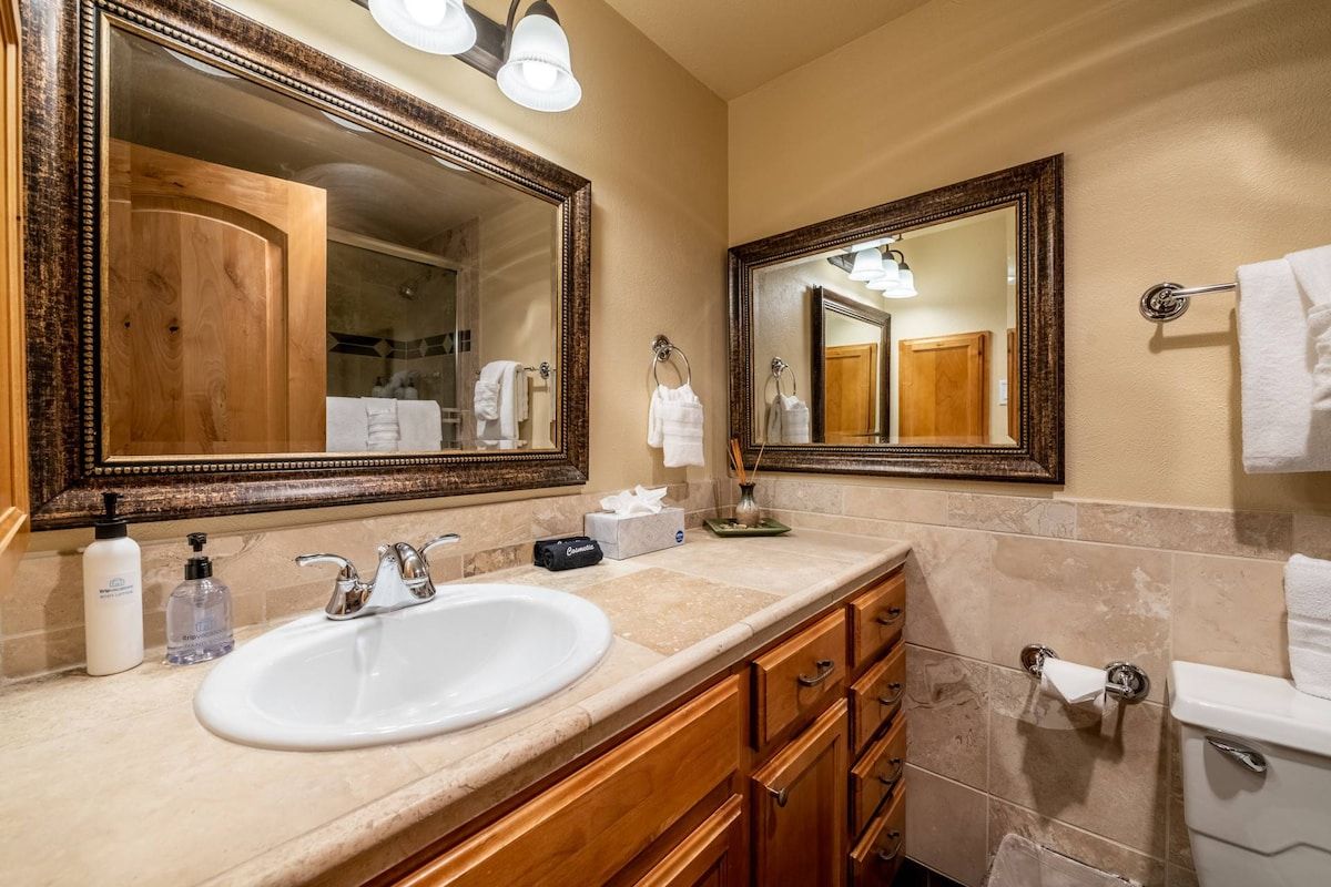 A bathroom with a large mirror, a sink, a toilet, and wooden cabinets.