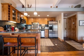 Una cocina moderna con armarios de madera, electrodomésticos de acero inoxidable y una isla central con taburetes de bar.