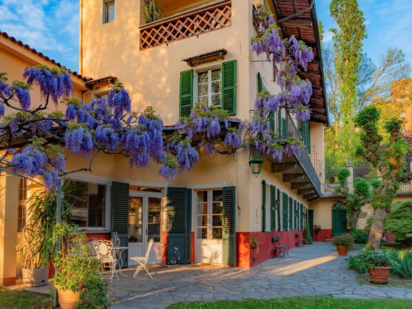 A building with a covered patio, green shutters, and purple flowering vines.
