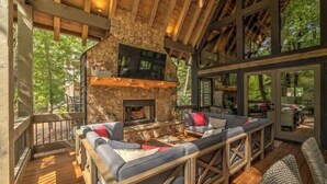 Un espacio de estar acogedor con chimenea de piedra, vigas de madera y un ventanal con vistas a la vegetación.