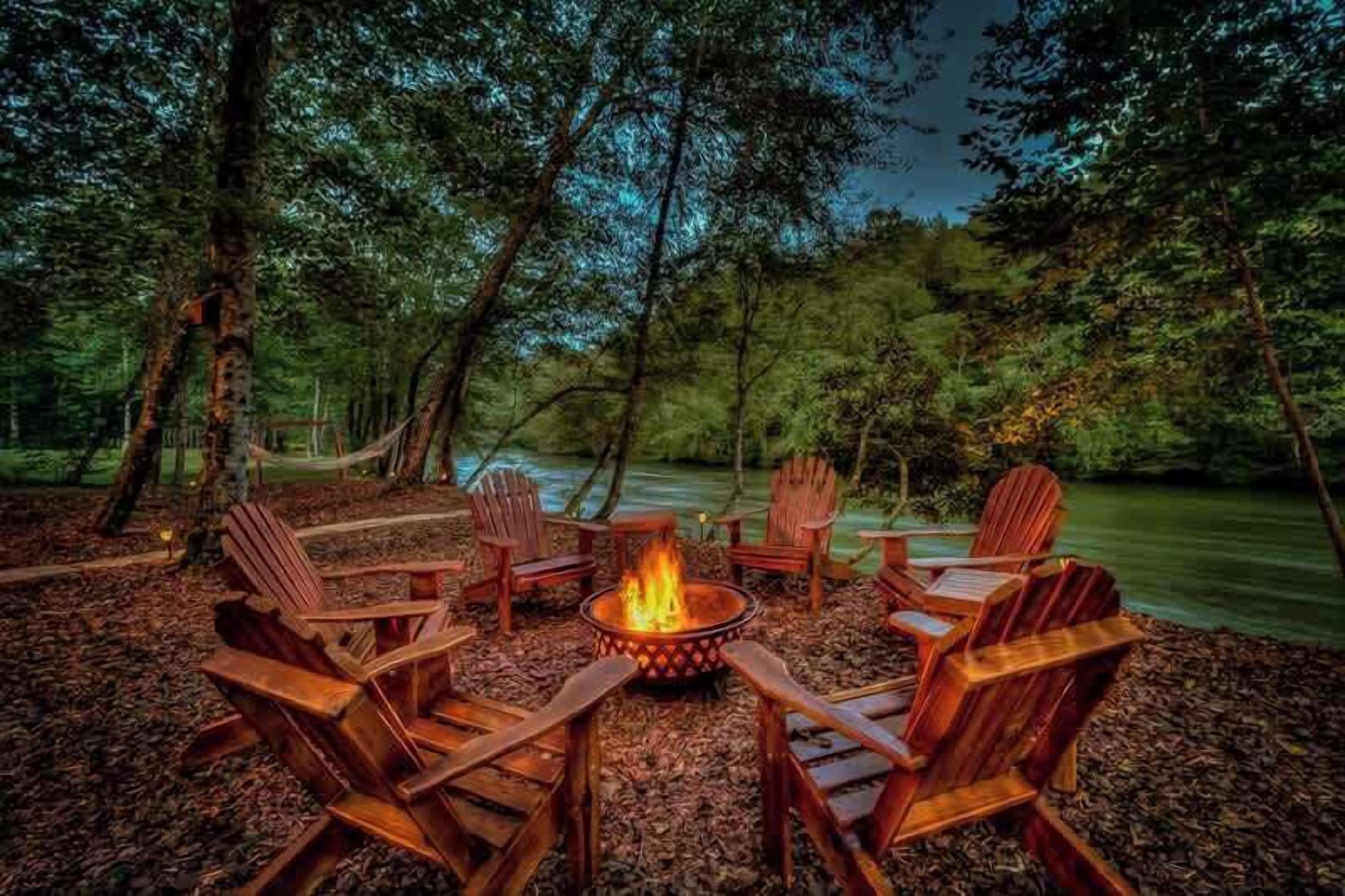 A campfire surrounded by wooden chairs in a forest setting.