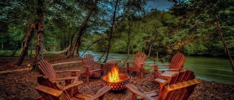 A campfire surrounded by wooden chairs in a forest setting.