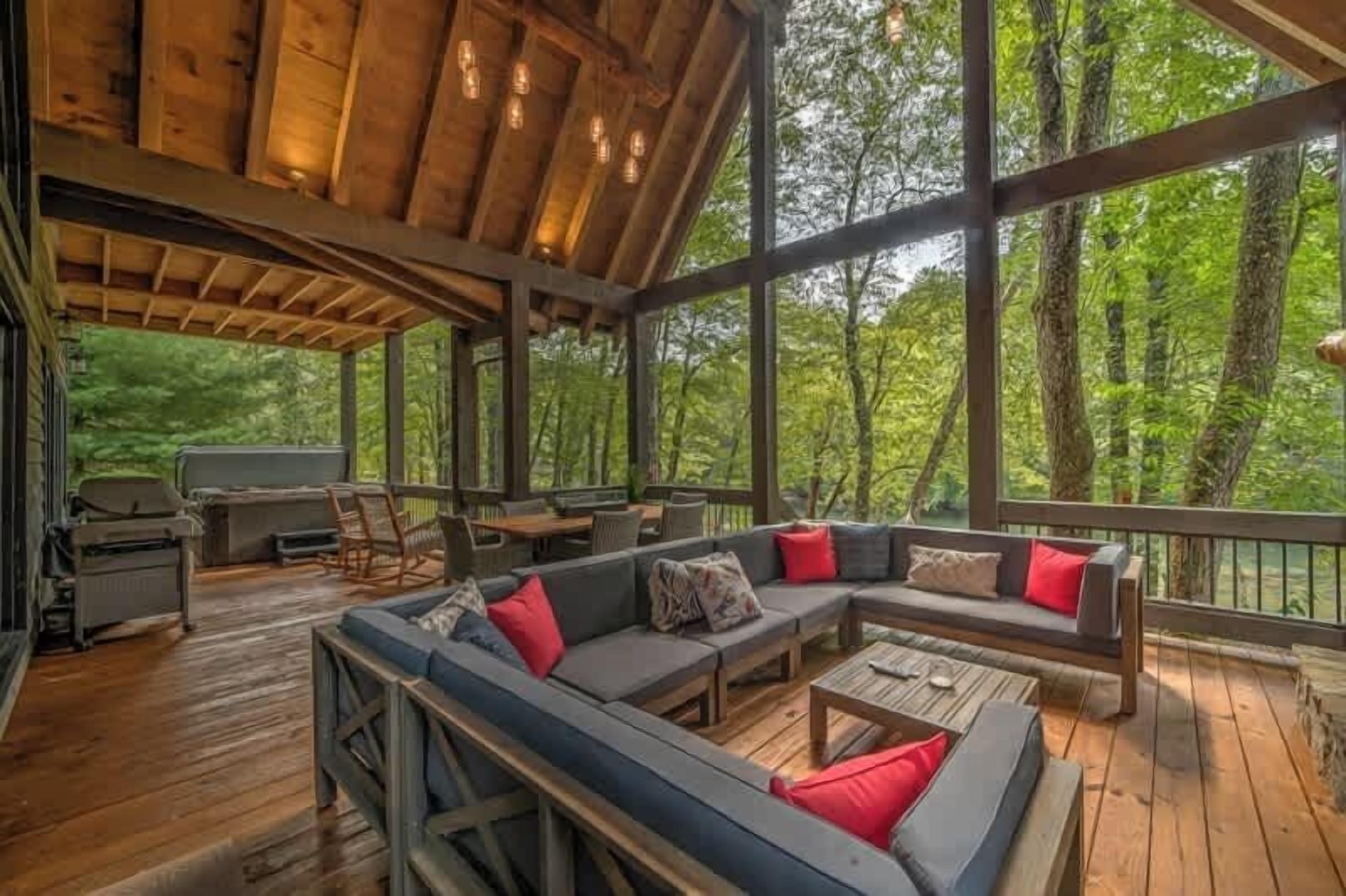 Un área de estar al aire libre techada con cubierta de madera, un sofá modular grande con cojines rojos y una parrilla.