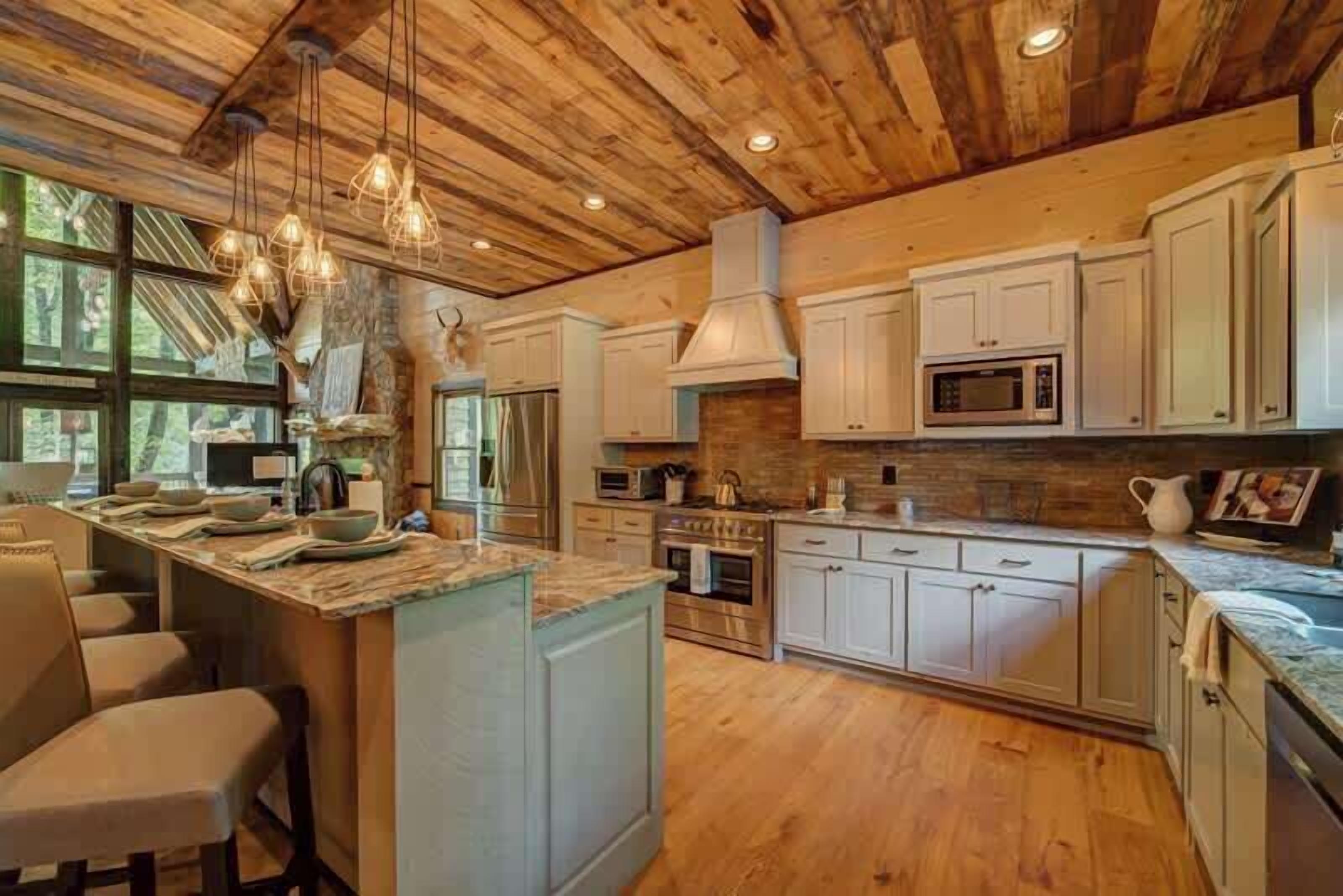 A kitchen with wooden ceiling, white cabinets, a central island, and pendant lighting.