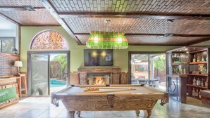 A pool table in a room with a brick ceiling, a fireplace, and a bar area with shelves of bottles. - Extraordinary Private Pool/Spa Villa w/man cave (Henderson)