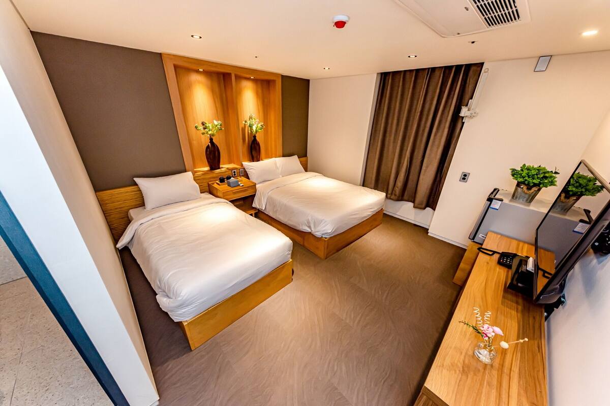 Een hotelkamer met twee bedden, een bureau met een computer, een spiegel en een kleine plant.