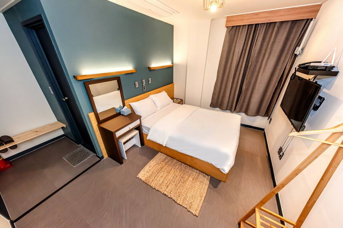Een hotelkamer met een bed, nachtkastjes, een bureau, een televisie en een raam met gordijnen.