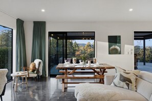 A modern interior with a dining area, a sofa, and a view of the outdoors. - Executive family house, private with stunning rural views close to Lake Rotoura (Rotorua)